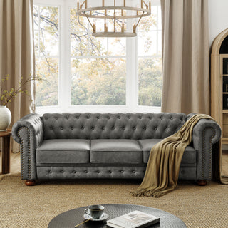 Gray tufted sofa in a living room with large windows and a chandelier.