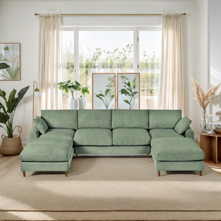 Green sectional sofa in a living room with plants and large windows.